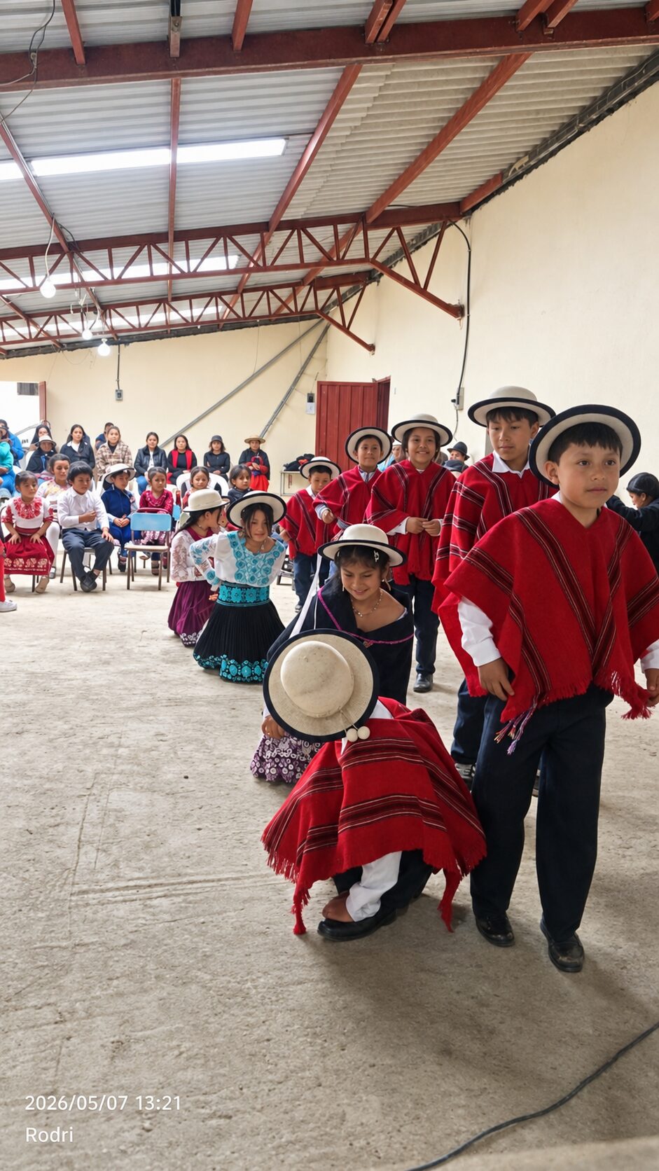 Niñas y niños participan en una presentación cultural andina dentro de un salón comunitario.