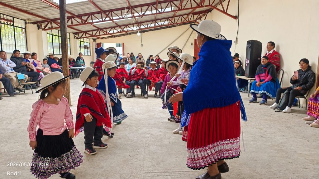 Niñas y niños participan en una presentación cultural andina dentro de un salón comunitario.