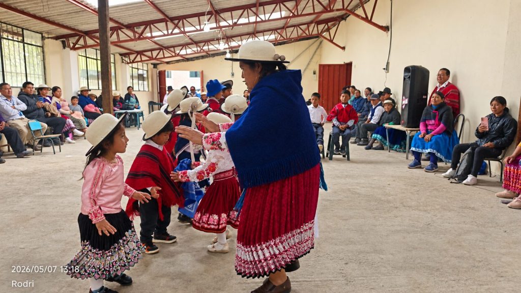 Niñas y niños participan en una presentación cultural andina dentro de un salón comunitario.