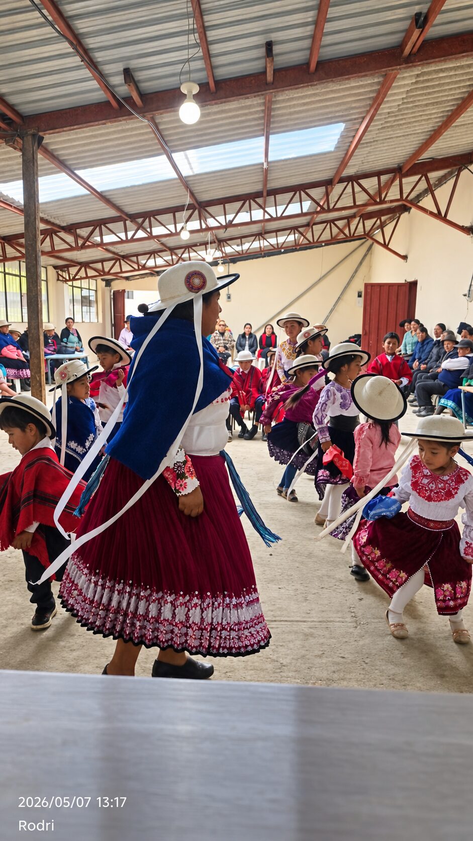 Niñas y niños participan en una presentación cultural andina dentro de un salón comunitario.